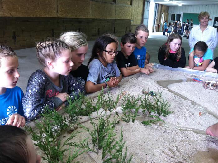 Kids stand around stream table while instructor shows them how water causes erosion.